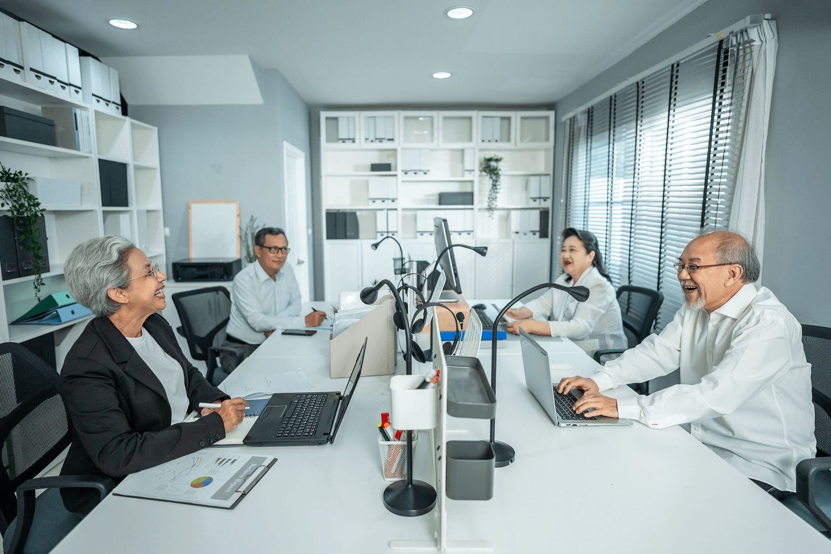 Elderly Asian business team collaborating in modern office, using laptops, smiling, teamwork, senior professionals.